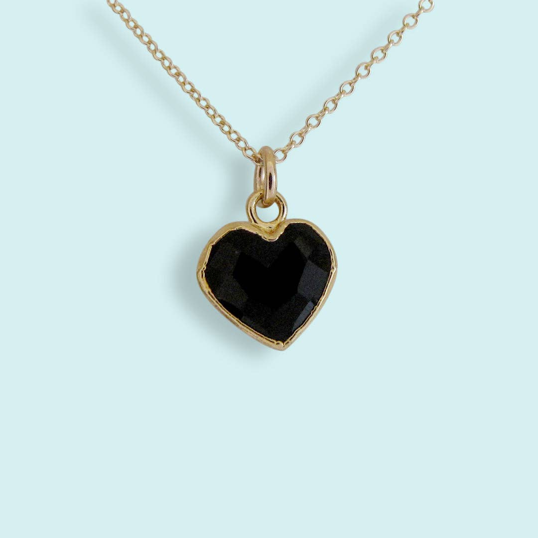 Heart-shaped black stone pendant on a gold chain against a light blue background