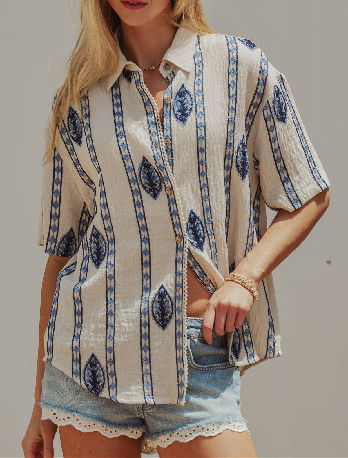 Woman wearing a patterned shirt and denim shorts against a plain background
