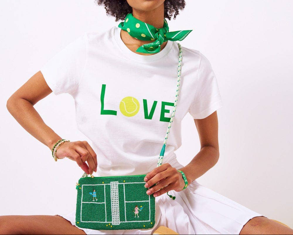 Woman wearing a white t-shirt with 'LOVE' and a green tennis ball graphic, holding a green handbag with a tennis court design.