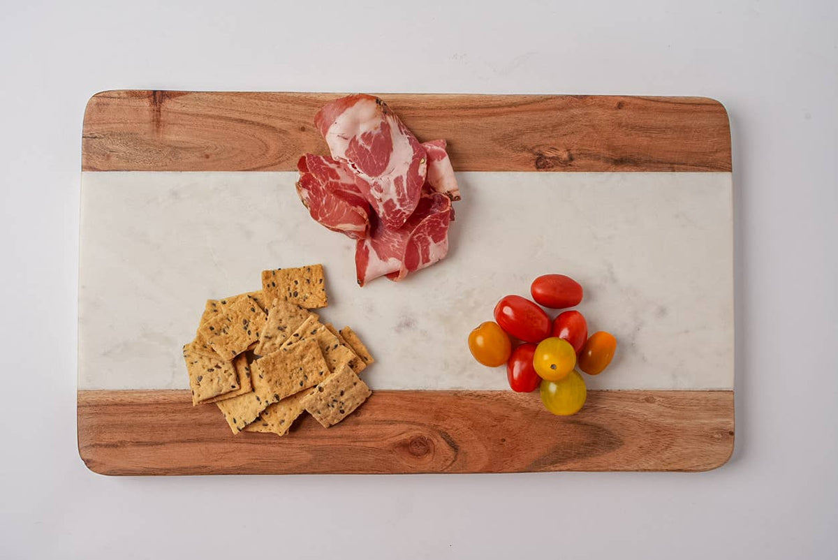 Wooden cutting board with sliced meat, crackers, and cherry tomatoes on a white background