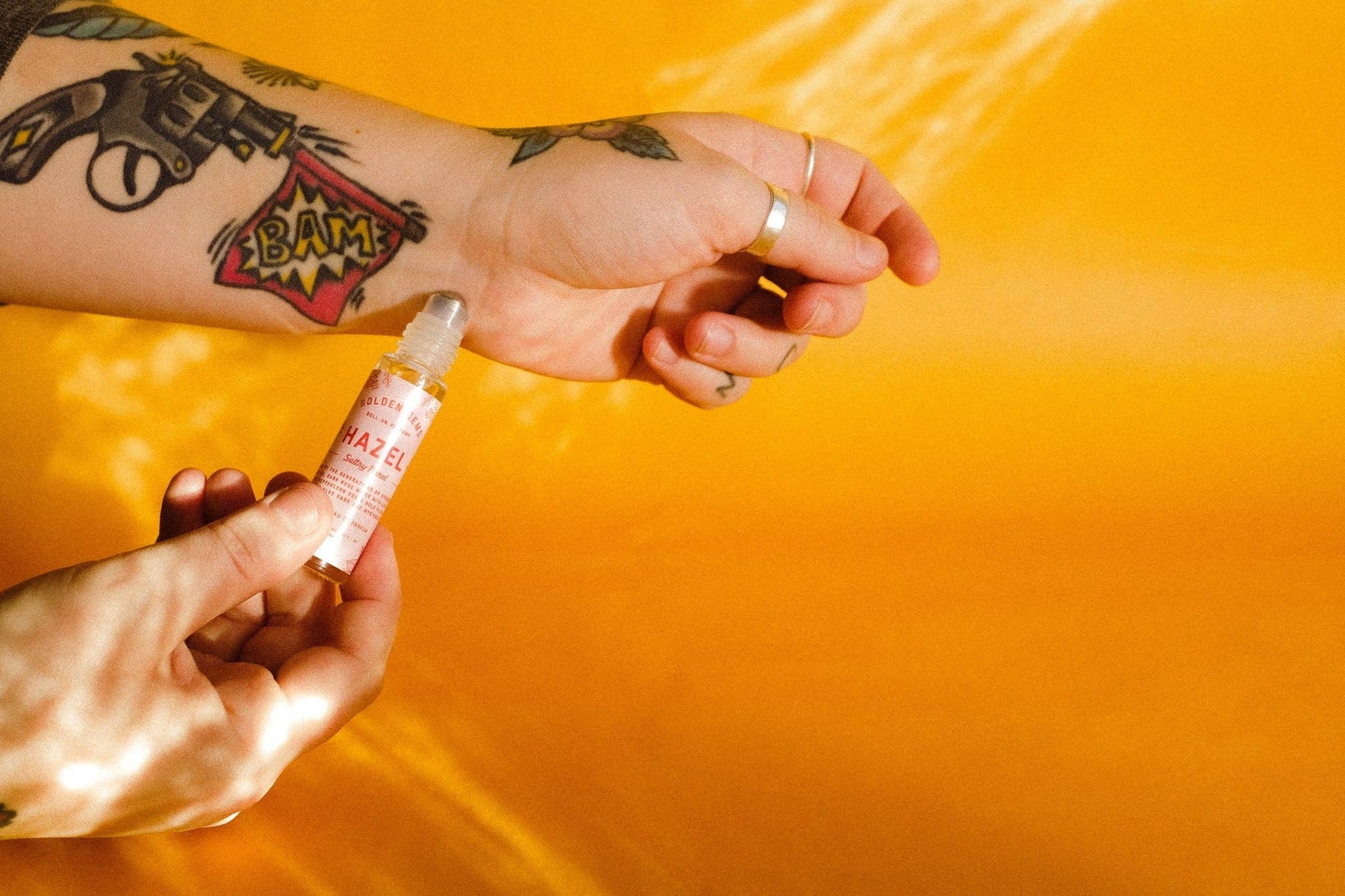 Hand applying a small bottle of product to another hand against an orange background