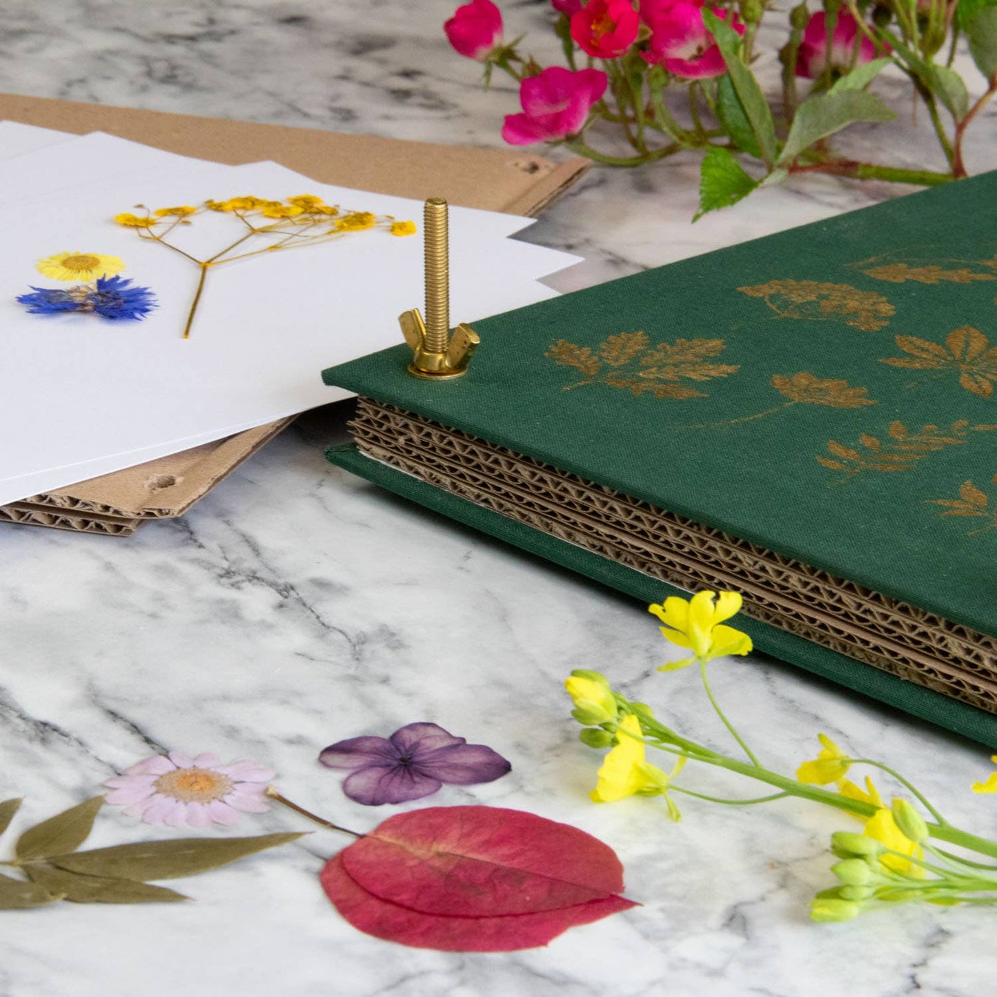 Green notebook with floral design on a marble surface with pressed flowers and a paper puncher.