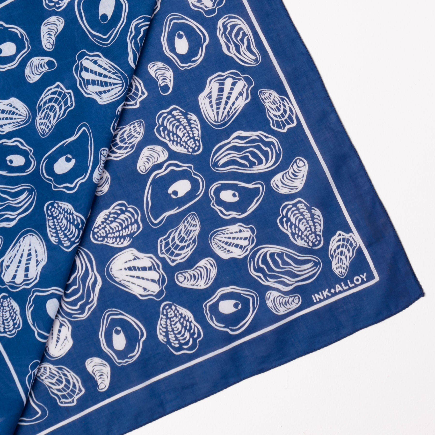 Blue bandana with white oyster shell pattern and 'INK+ALLOY' branding.