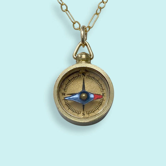 Brass compass pendant on a chain against a light blue background