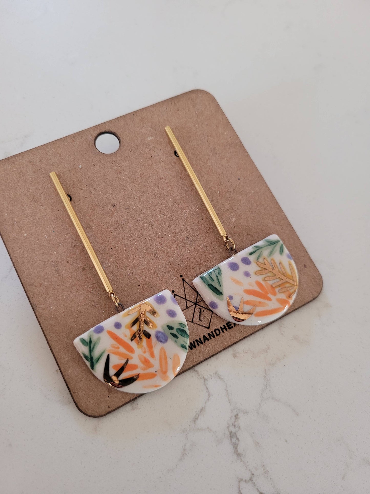 Pair of floral earrings on a brown card with 'MADAME' branding, on a marble surface.