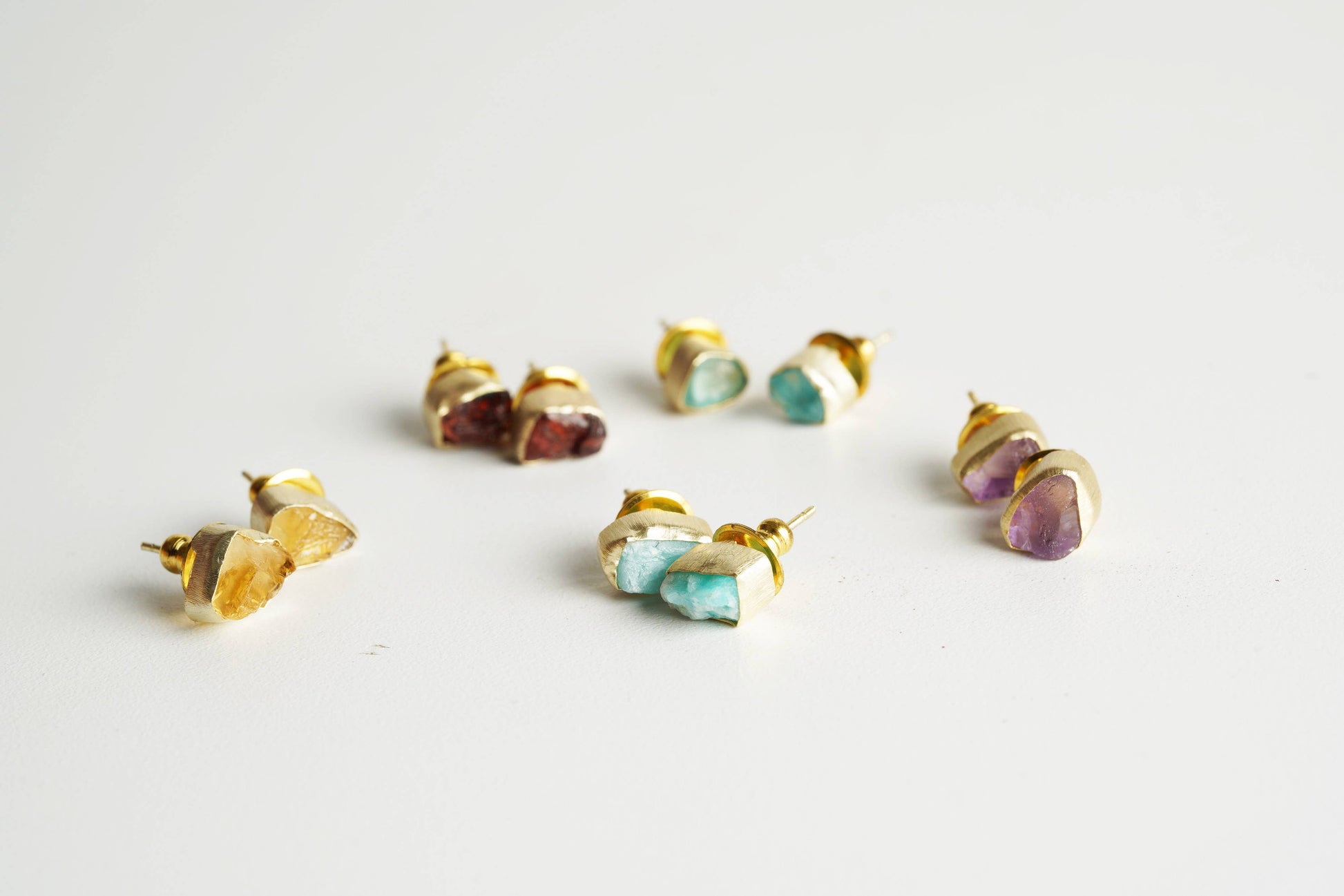 Gold-framed gemstone stud earrings on a light gray background