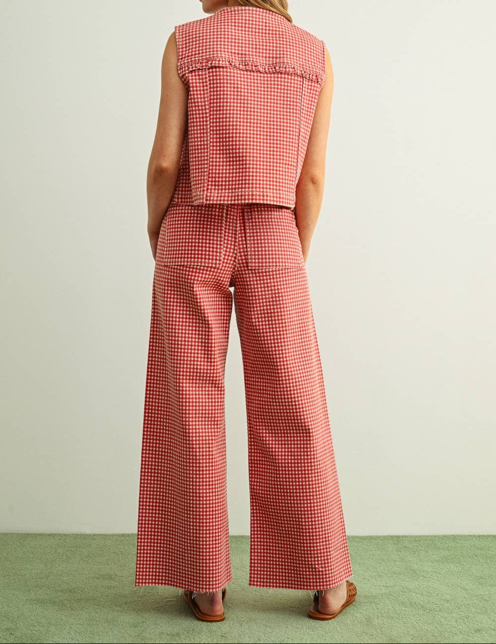 Woman wearing a red checkered outfit with wide-leg pants on a light green floor and white wall background.