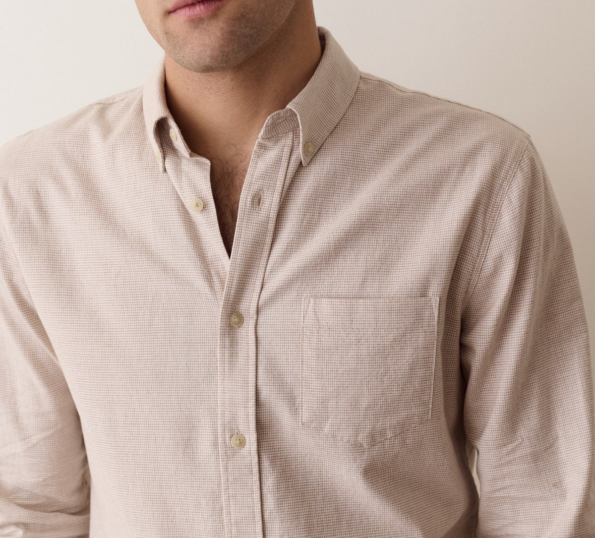 A close-up shot of a man wearing a light beige textured long-sleeve button-down shirt against a plain off-white background.