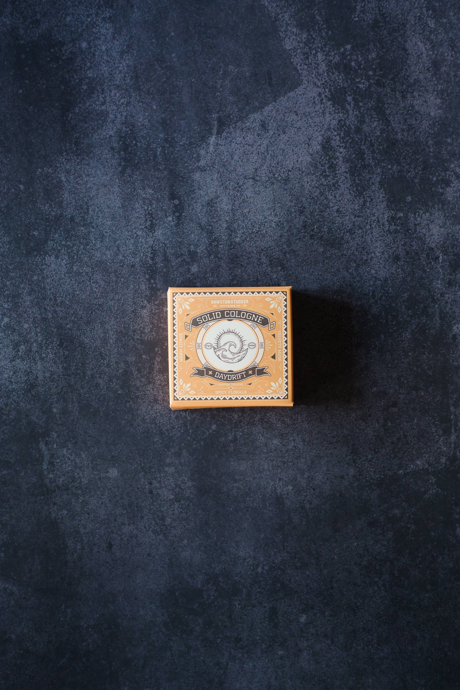 Small leather box with a brand logo on a dark textured surface