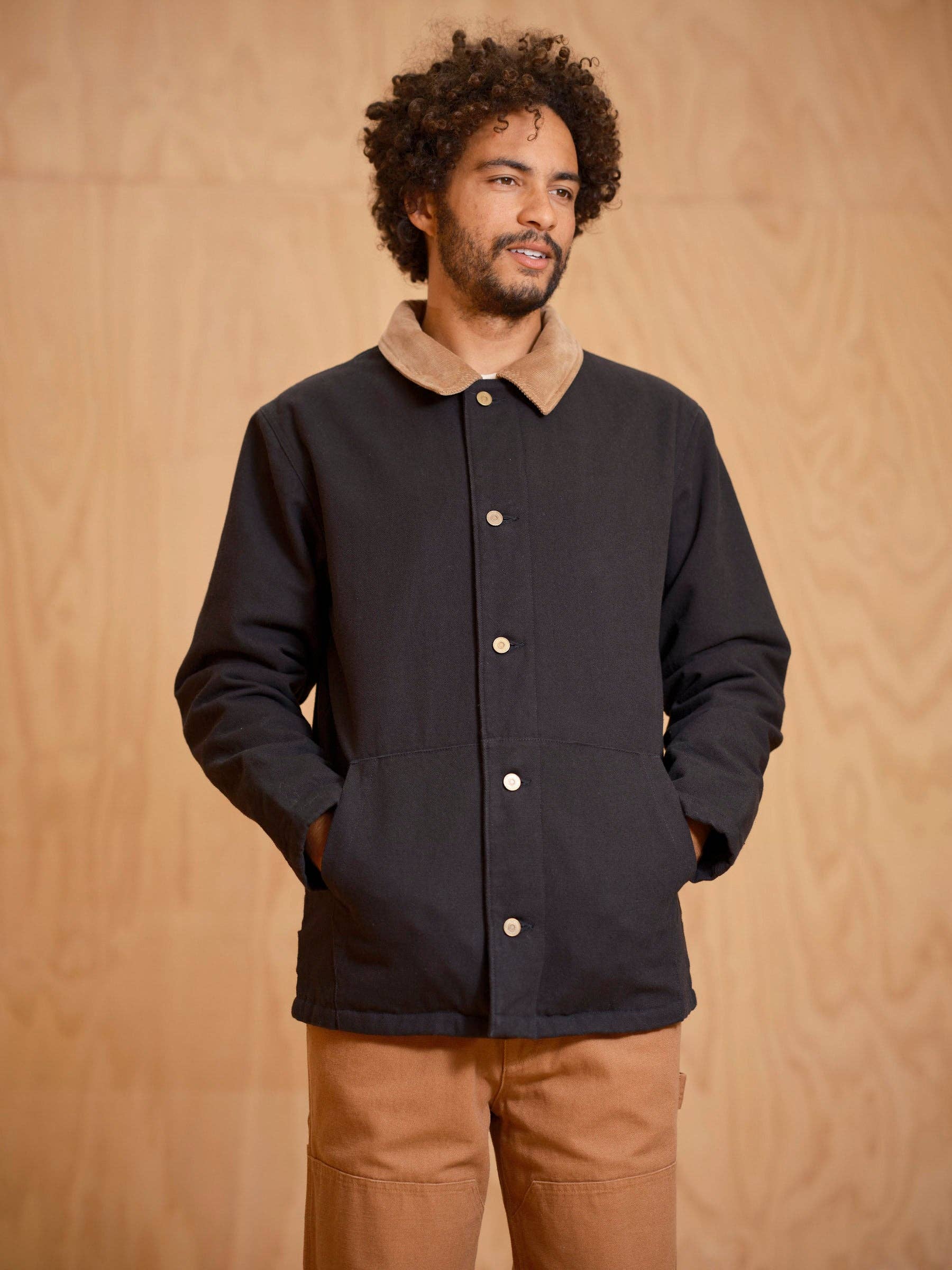 Man wearing a black jacket with a brown collar against a beige background