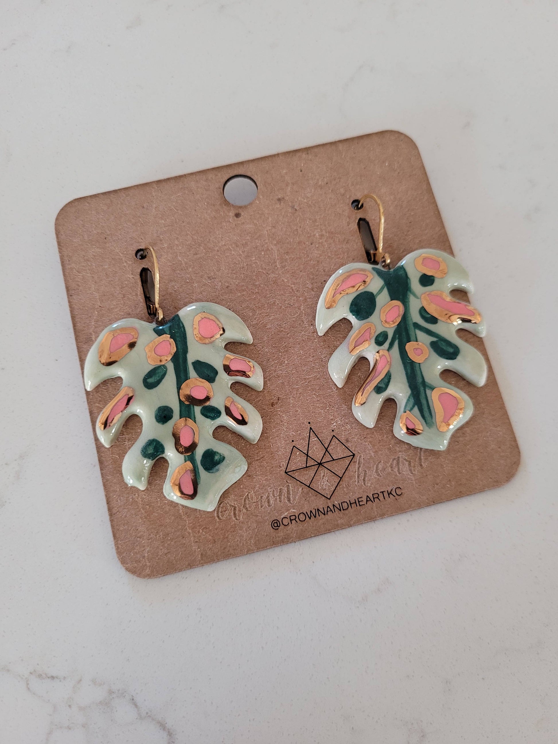 Pair of leaf-shaped earrings on a cardboard backing with a brand logo.
