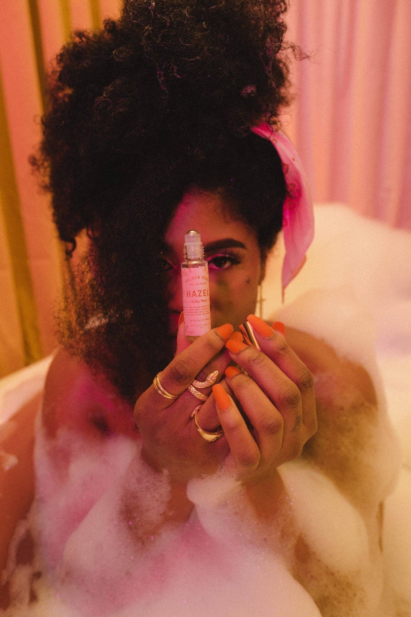 Person holding a pink bottle in a bubble bath setting