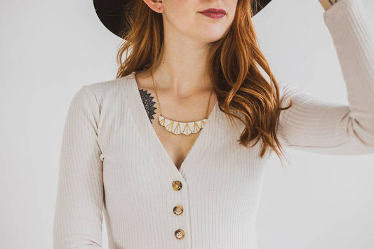 Woman wearing a beige cardigan with gold buttons and a necklace, against a plain background
