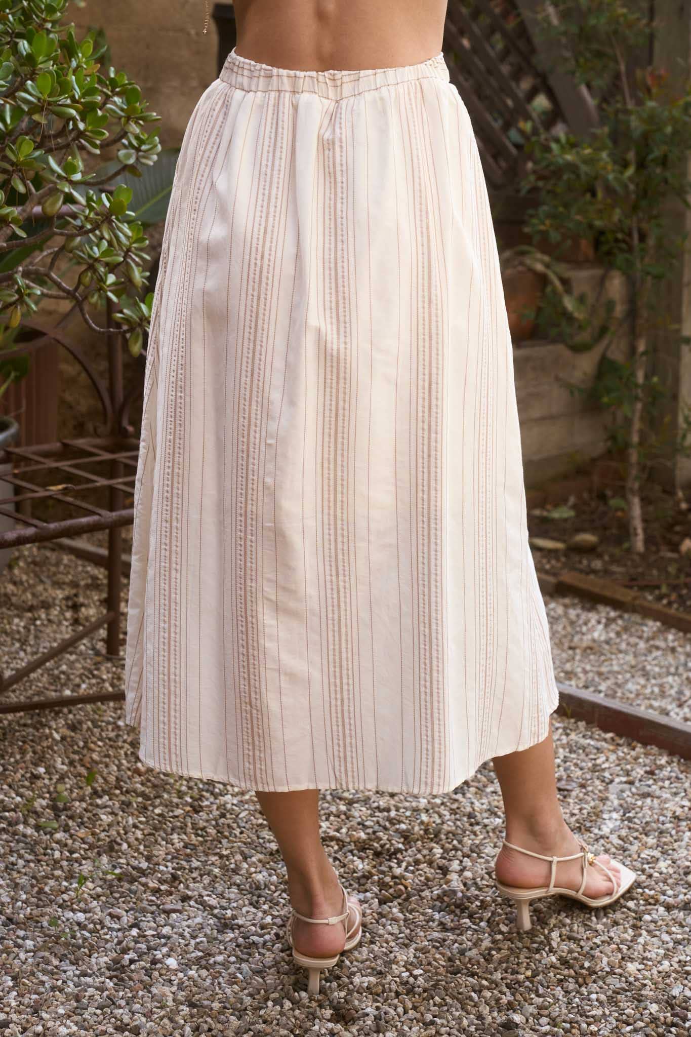 Person wearing a beige pleated skirt outdoors with plants in the background