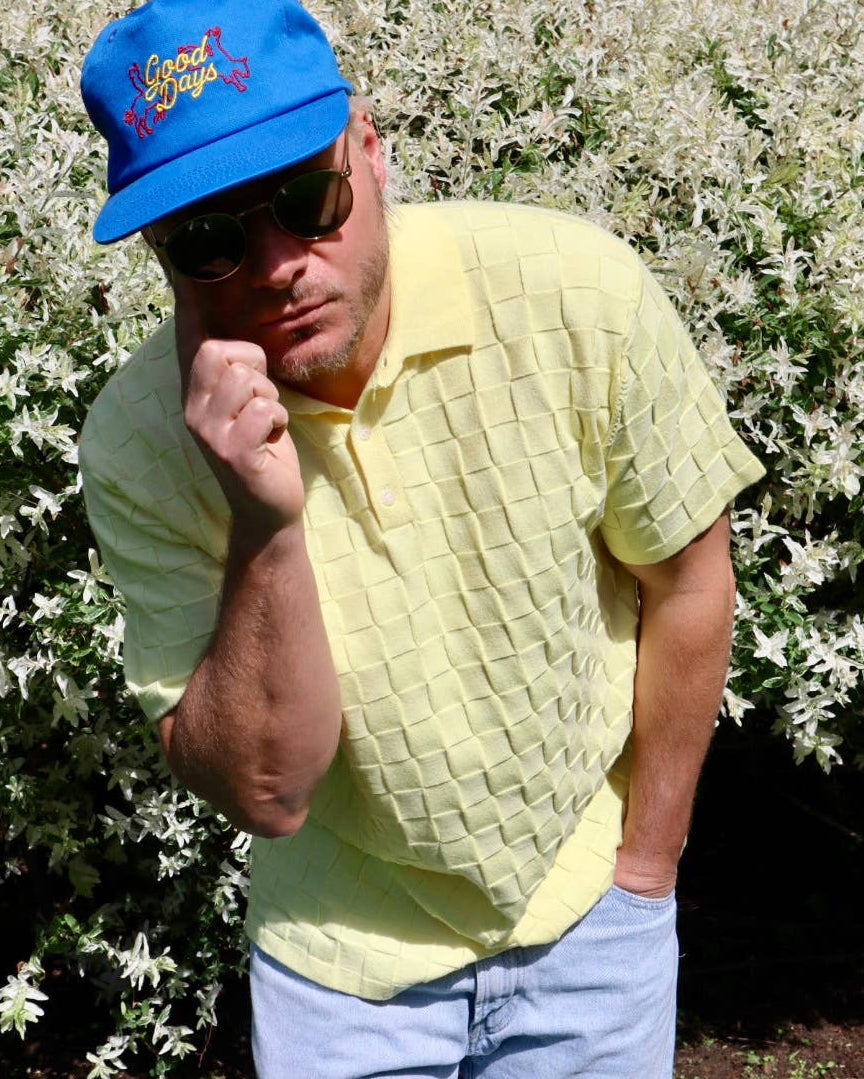 Man in a yellow shirt and blue cap standing in front of a white flowering bush