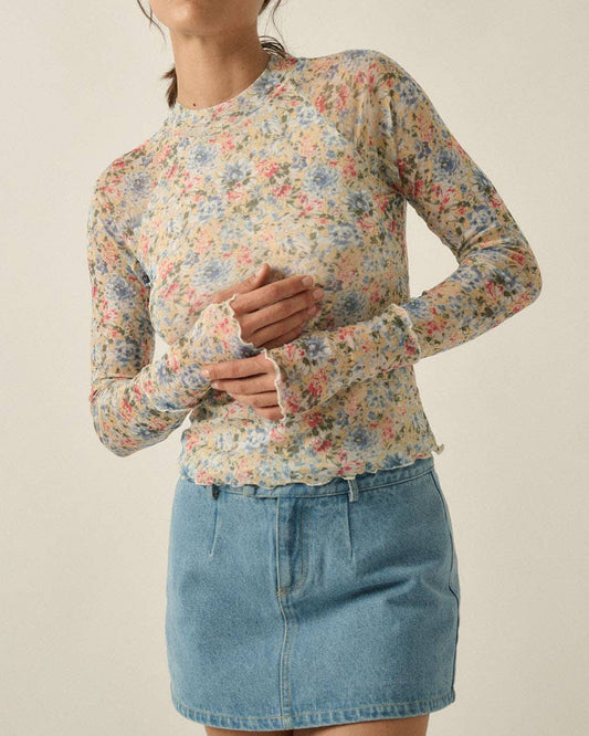 Woman wearing a floral top and denim skirt on a beige background