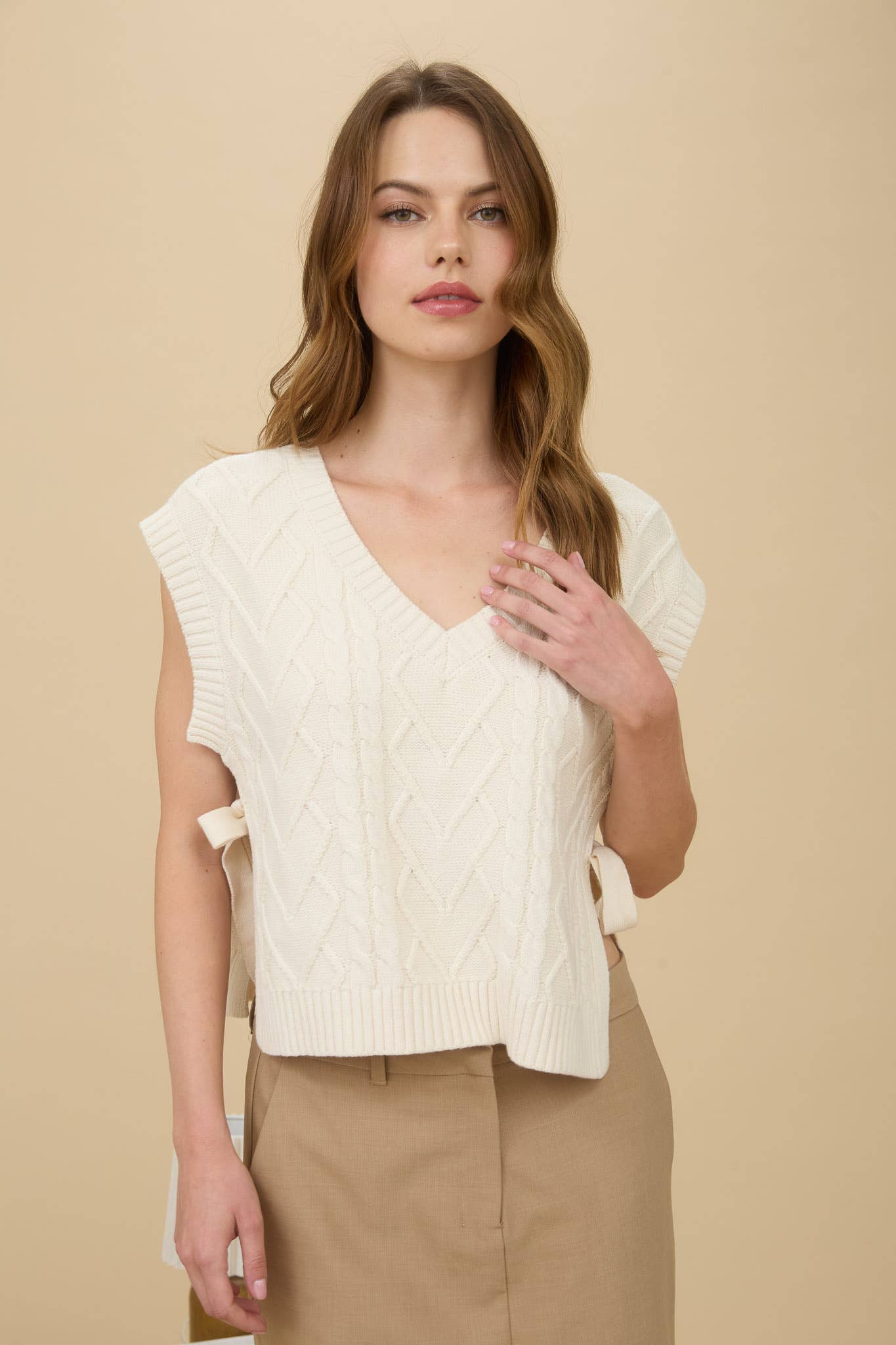 Woman wearing a cream-colored knitted vest against a beige background