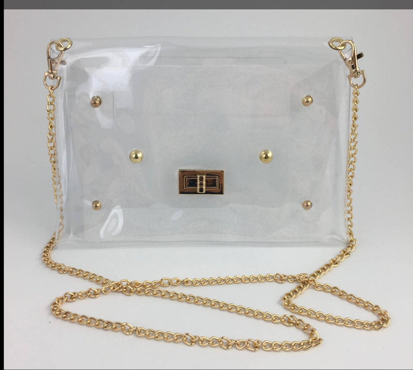 A clear vinyl shoulder bag with gold-tone hardware, including a chain strap, gold studs, and a central metal clasp, shown on a plain light background.