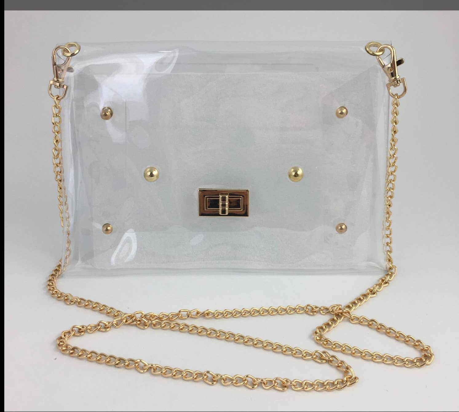 A clear vinyl shoulder bag with gold-tone hardware, including a chain strap, gold studs, and a central metal clasp, shown on a plain light background.