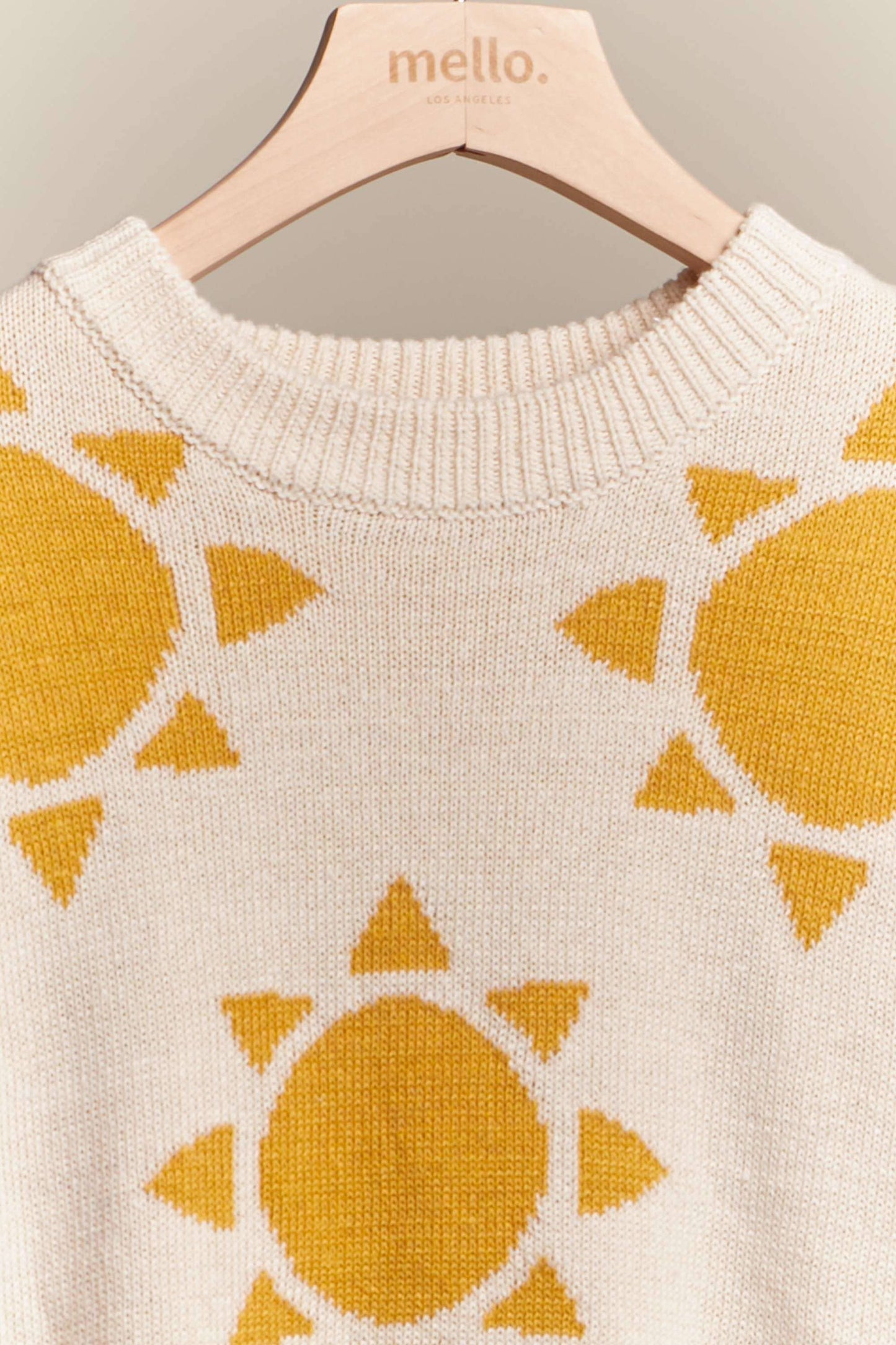 Beige sweater with yellow sun patterns on a hanger.