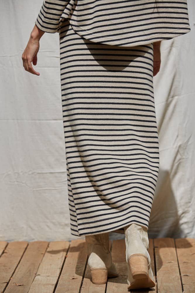 Person wearing a black and white striped dress with beige shoes on a wooden floor.