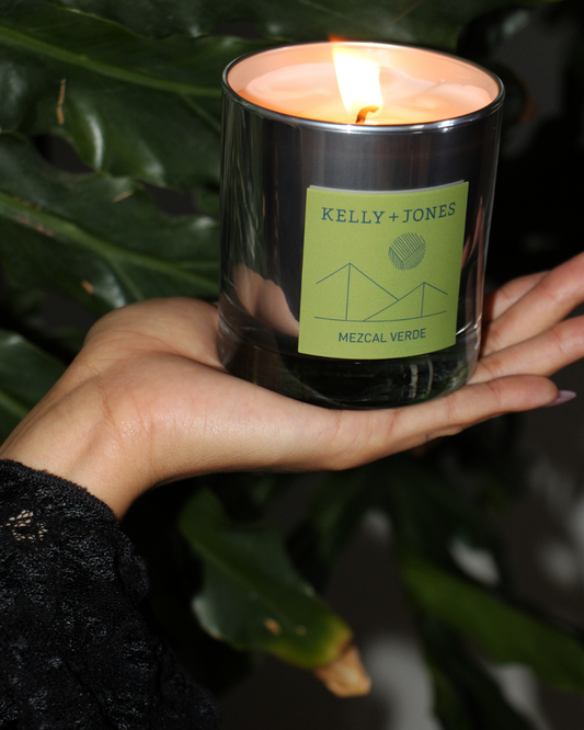 Hand holding a Kelly + Jones candle with a green label against a leafy background