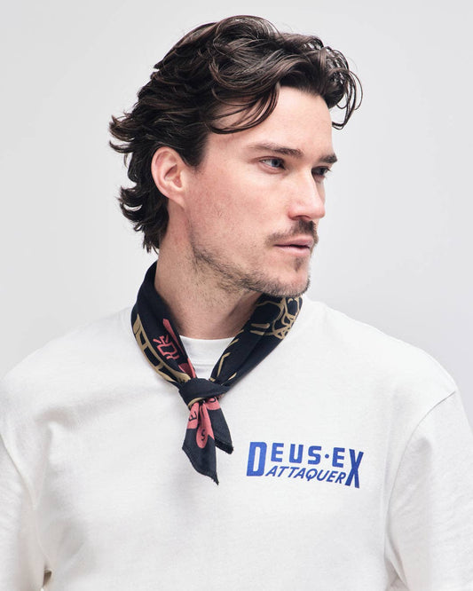 Man wearing a white shirt with 'Deus Ex Attaquer' text and a black scarf with colorful patterns.