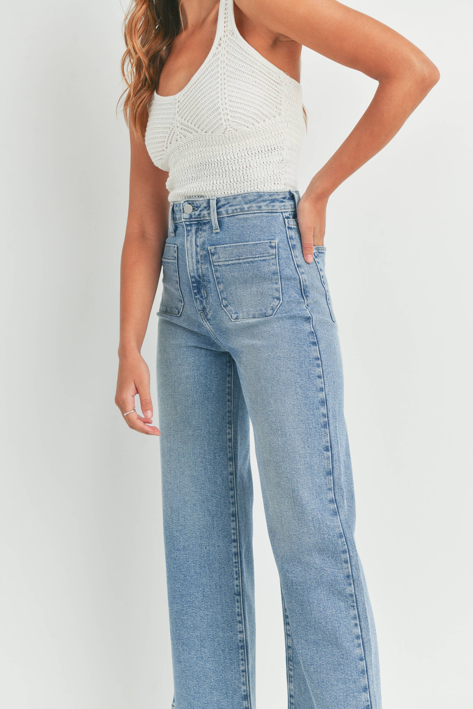 Person wearing light blue jeans and a white top against a plain background