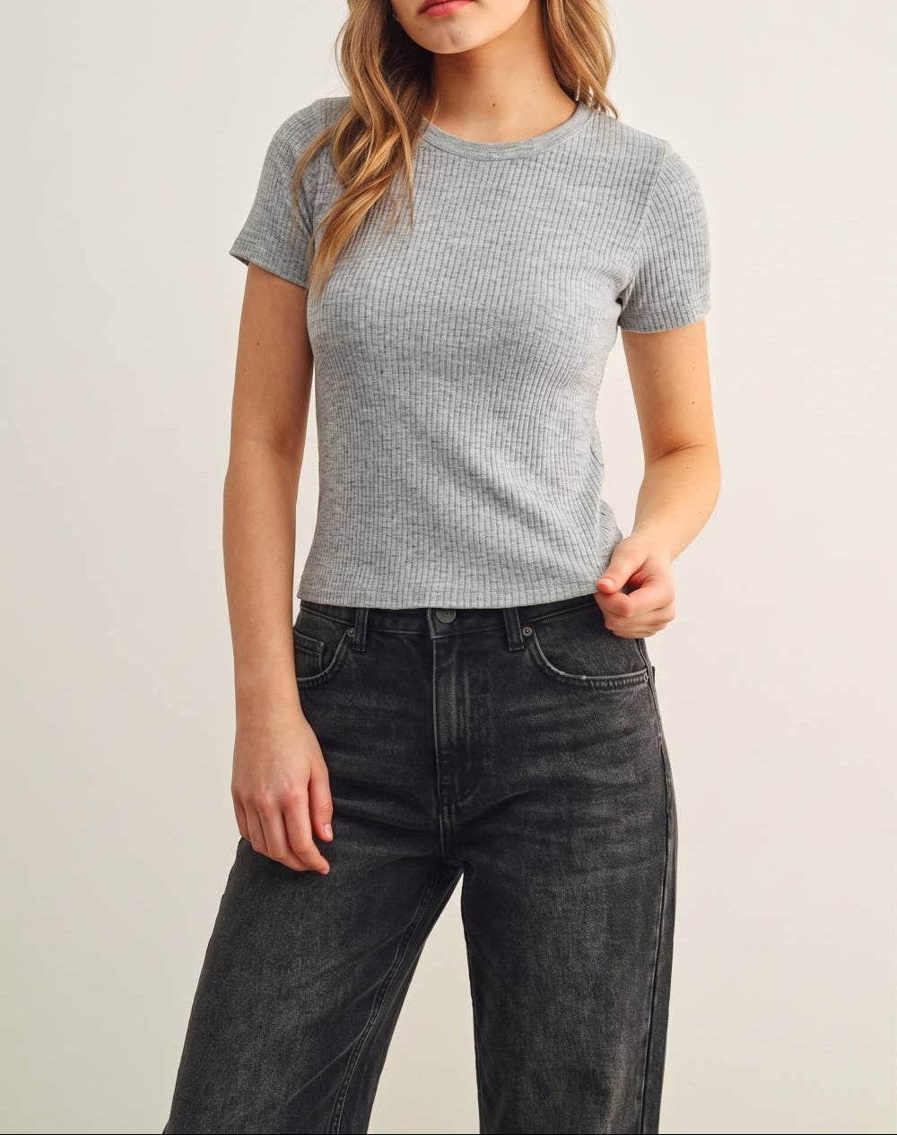 Woman wearing a gray ribbed t-shirt and black jeans on a plain background
