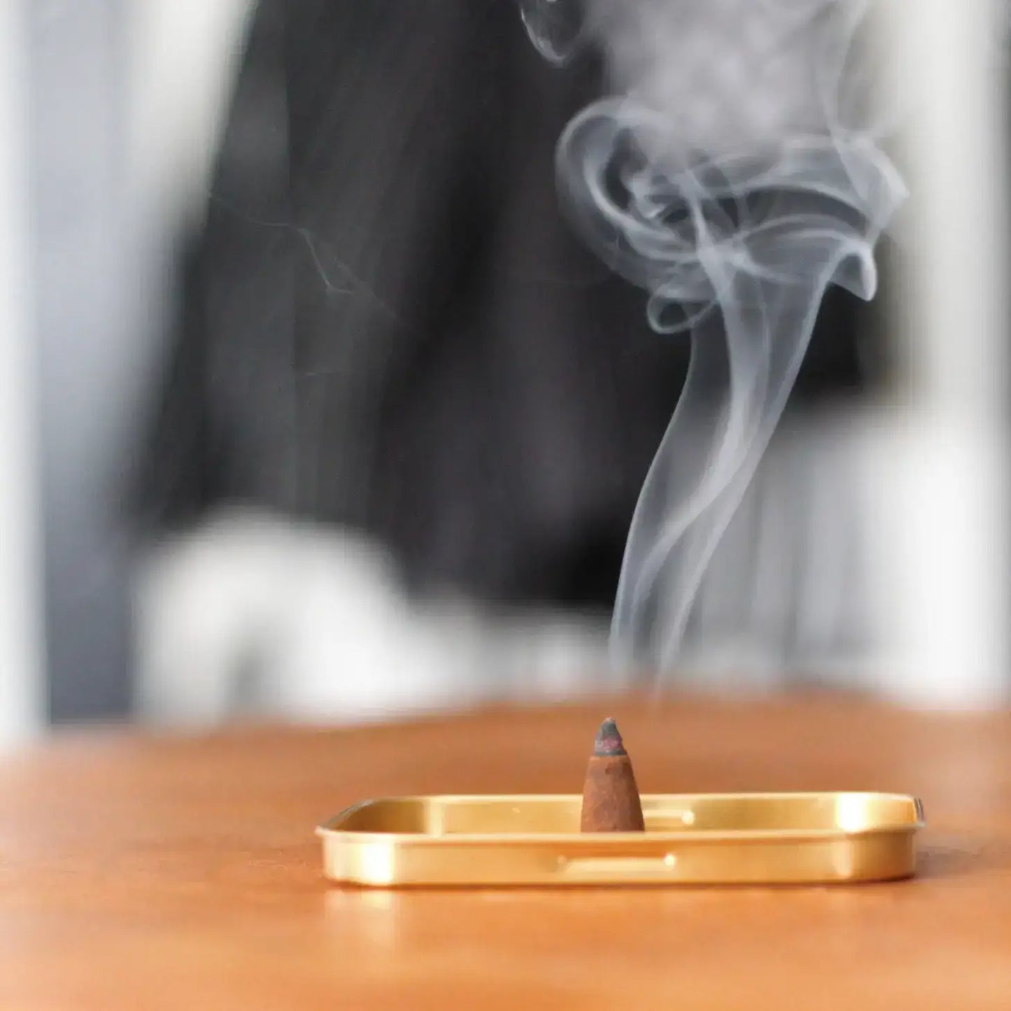 Incense cone burning on a wooden tray with smoke rising against a blurred background