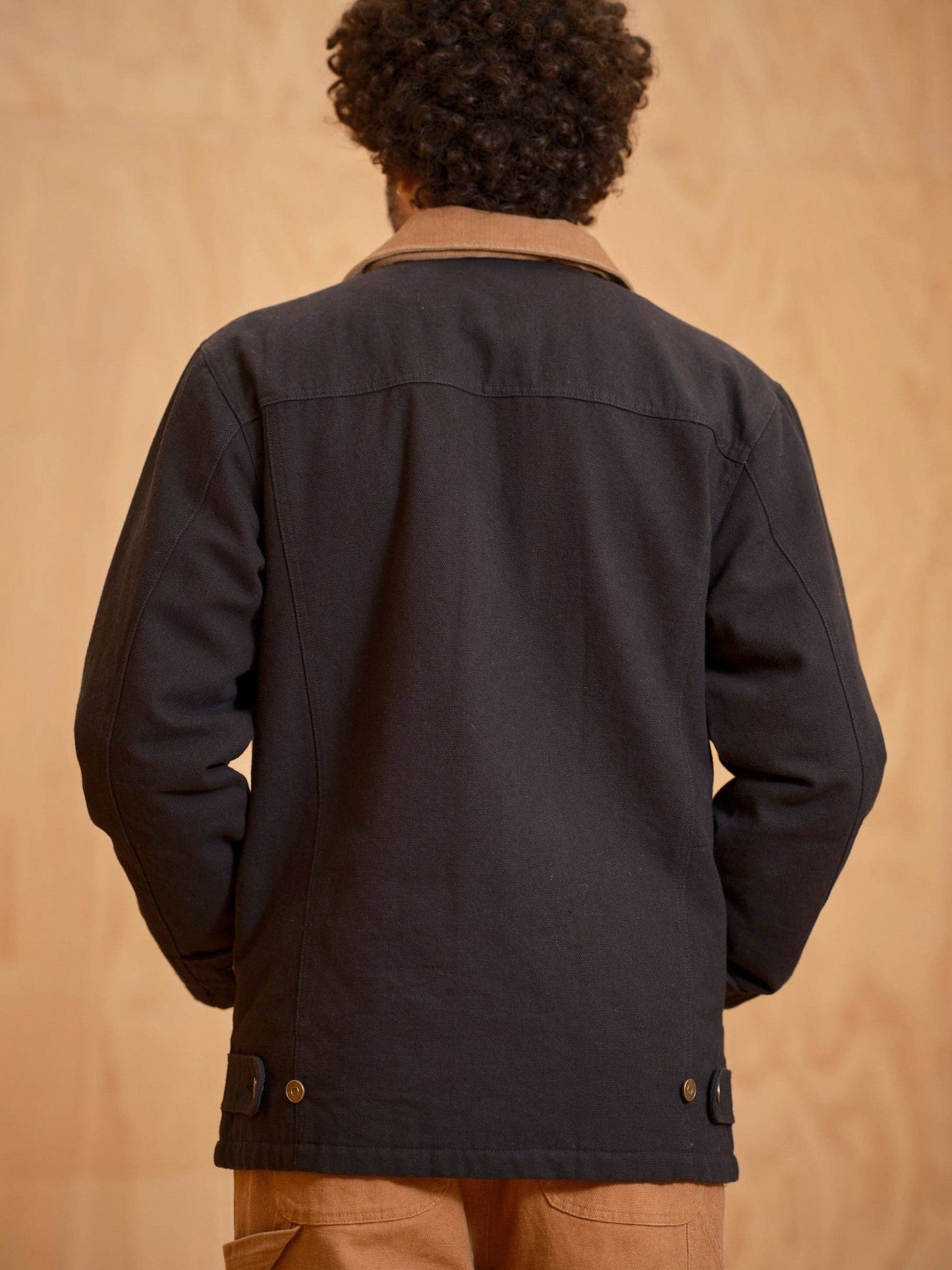 Person wearing a black jacket with a beige background