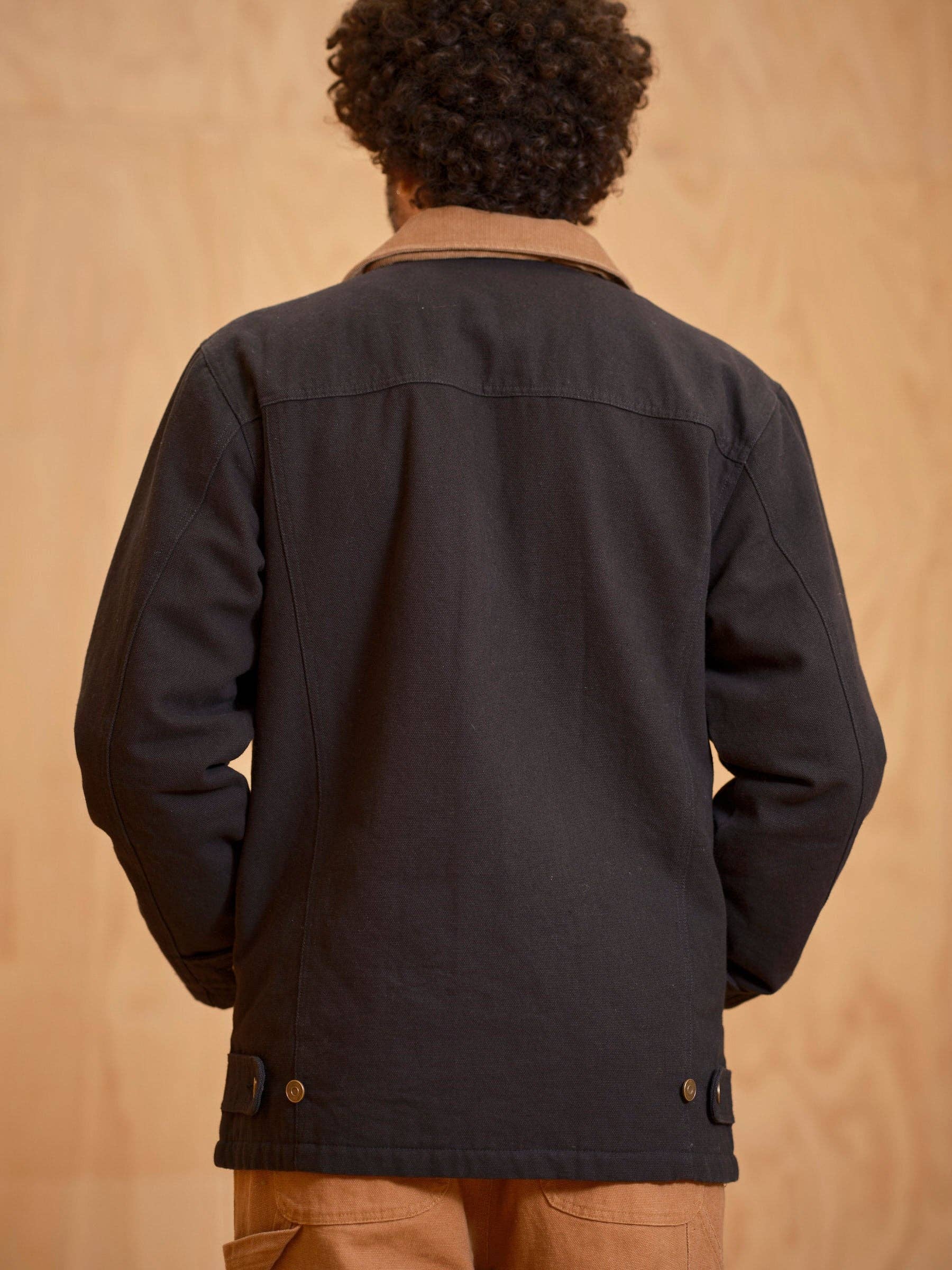 Person wearing a black jacket with a beige background