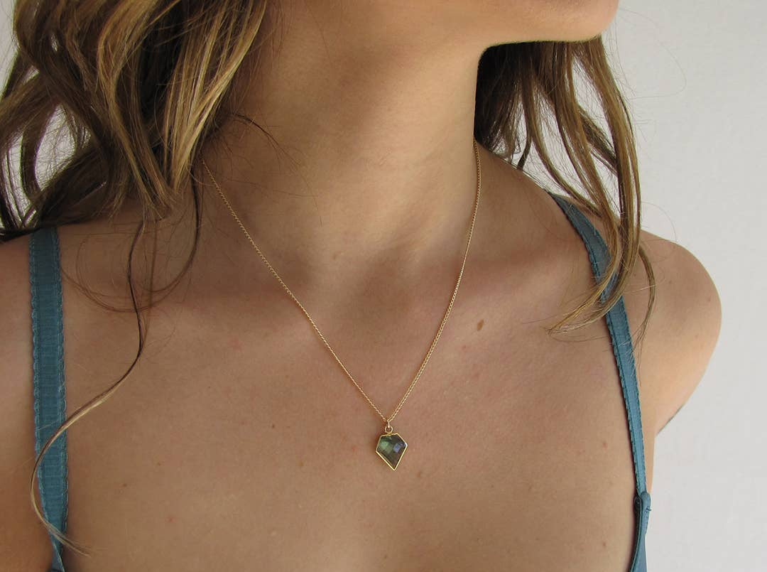 Woman wearing a gold necklace with a green pendant against a neutral background