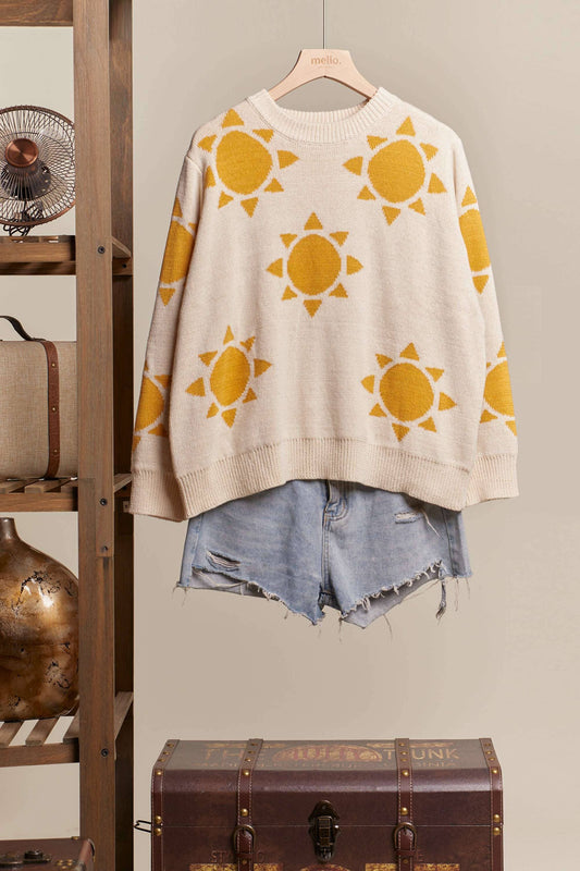 Beige sweater with yellow sun patterns hanging on a wooden rack with denim shorts below.
