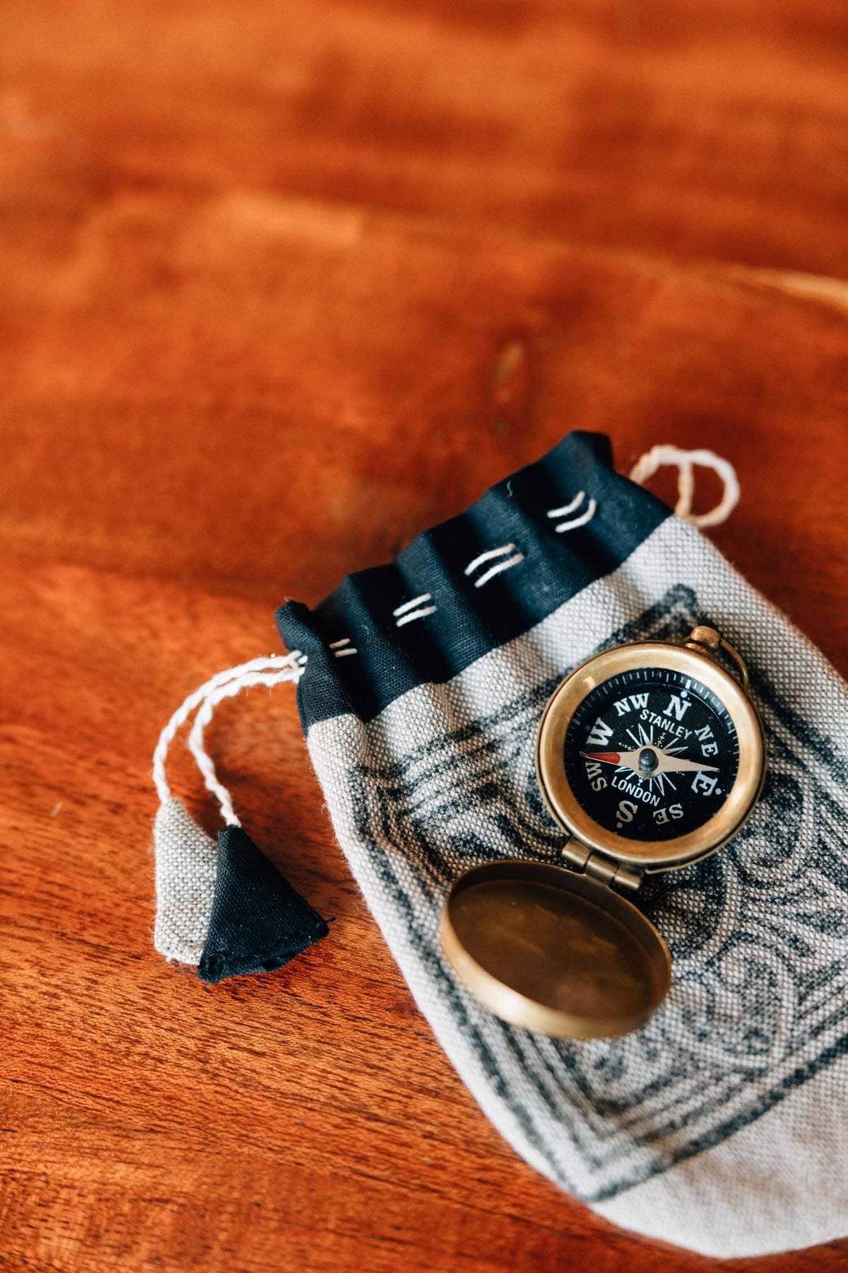 Small compass on a decorative pouch with tassels on a wooden surface