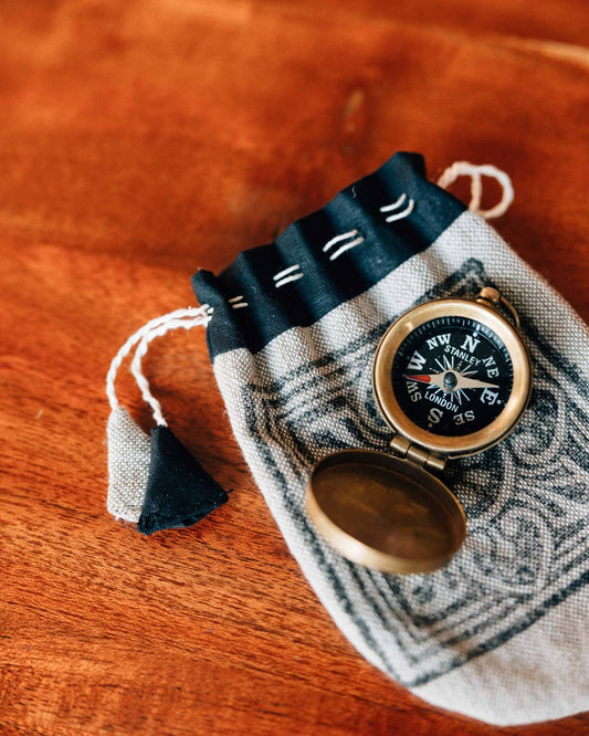 Small compass on a decorative pouch with tassels on a wooden surface
