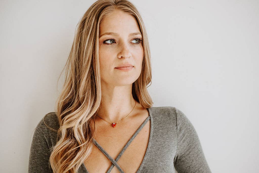 Woman wearing a gray top with a red necklace against a plain background