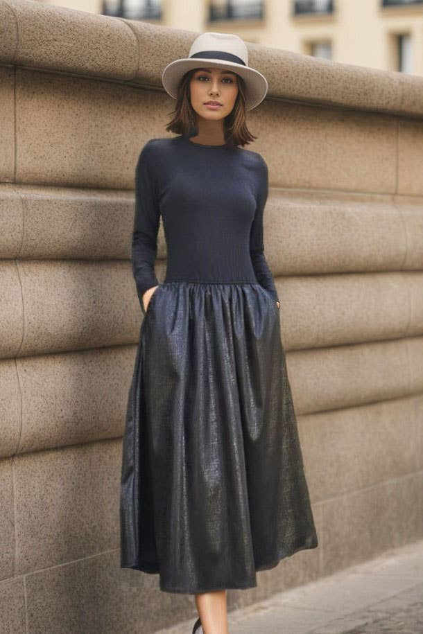 Woman wearing a dark blue dress and hat against a stone wall.