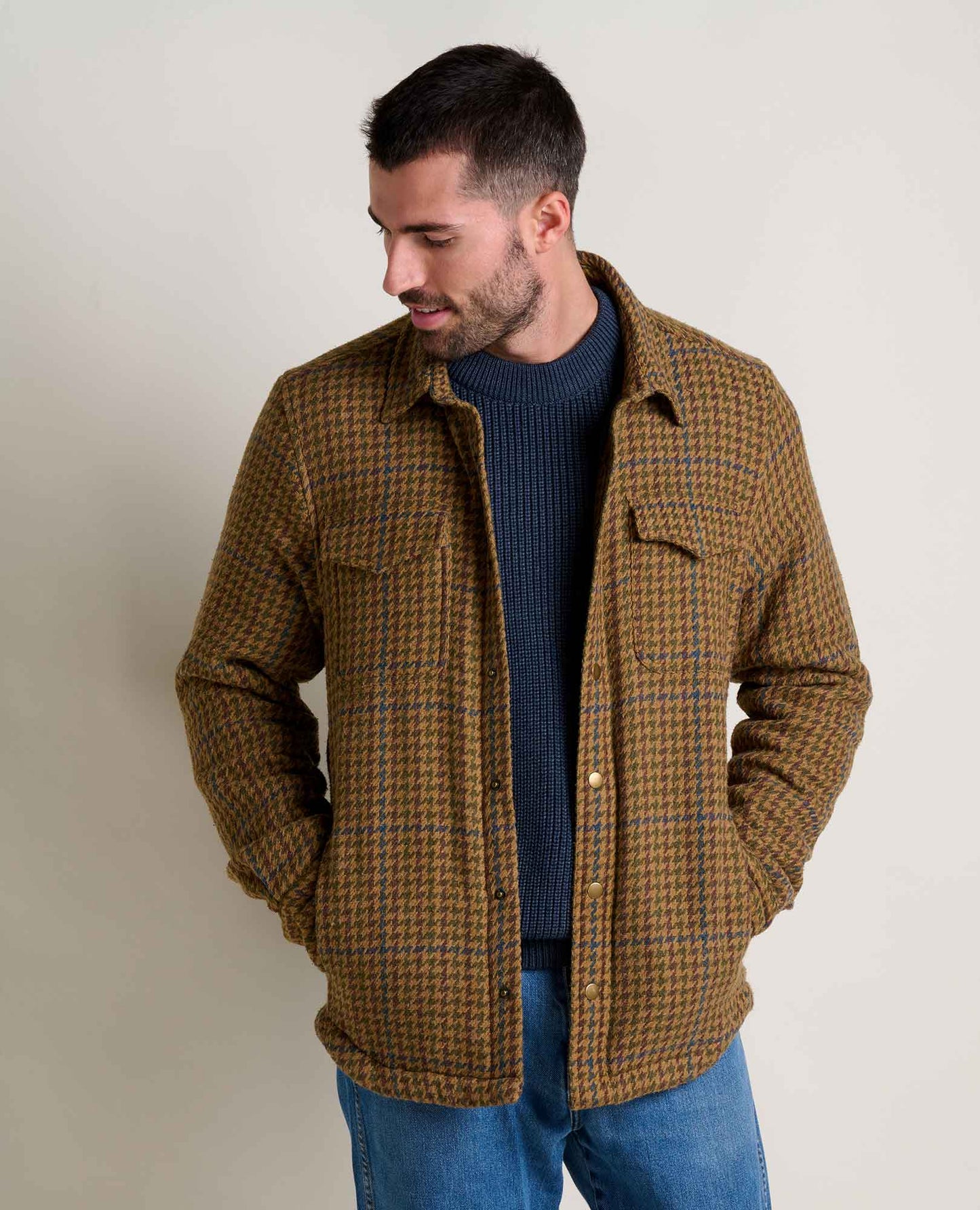 Man wearing a brown plaid jacket over a blue sweater against a plain background