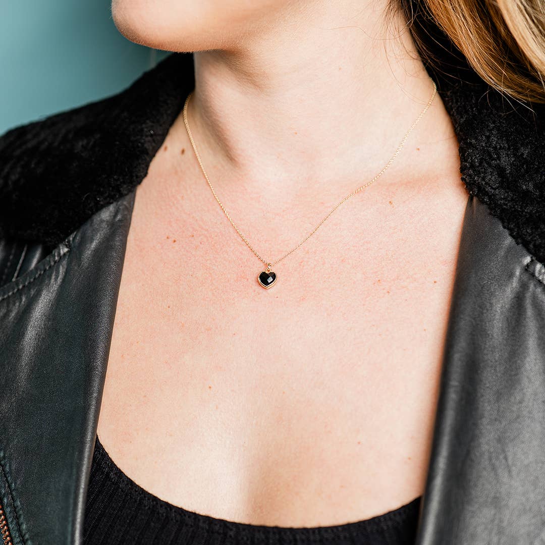 Person wearing a necklace with a heart pendant on a neutral background