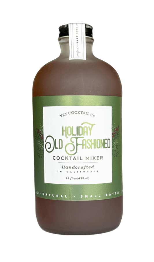 A bottle of Yes Cocktail Co. Holiday Old Fashioned Cocktail Mixer, featuring a brown liquid inside a clear glass bottle with a green and white label, set against a plain white background.