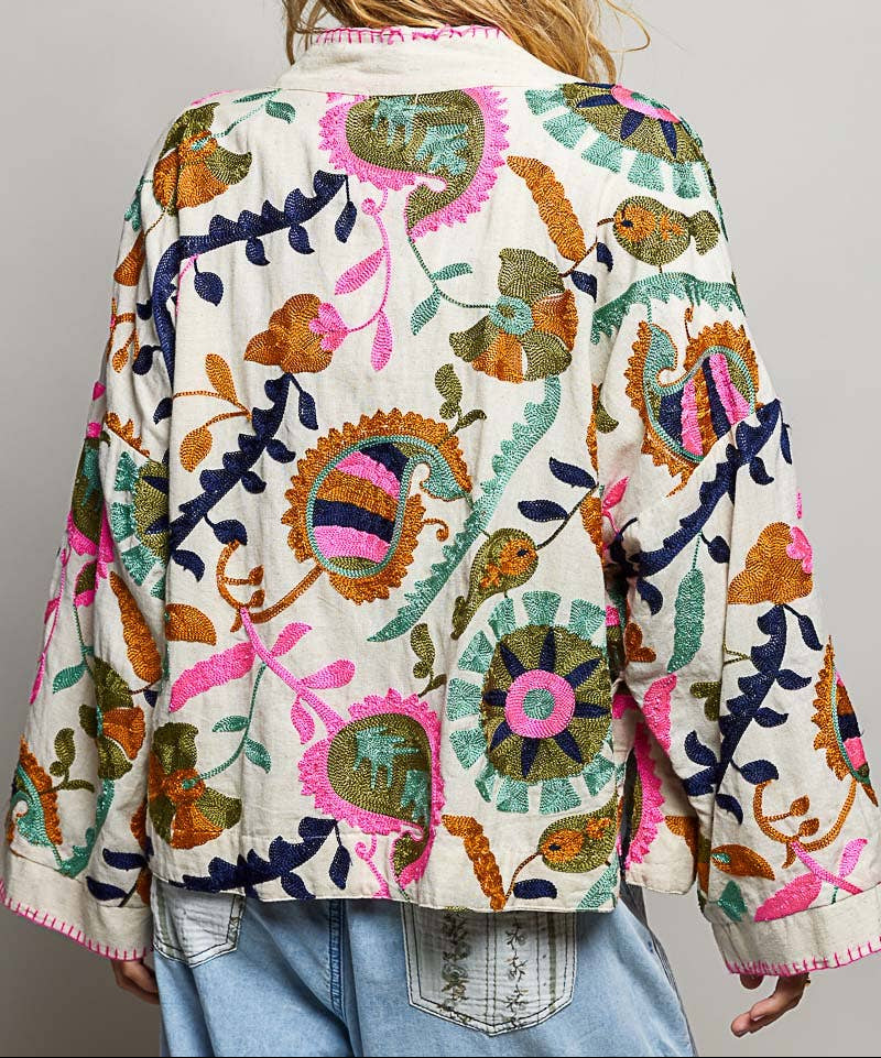 Person wearing a colorful embroidered jacket with a neutral background