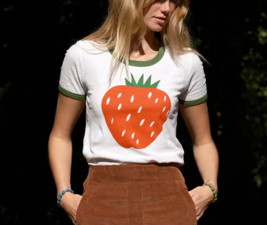 A person wearing a white t-shirt with a large green and orange strawberry graphic on the front.