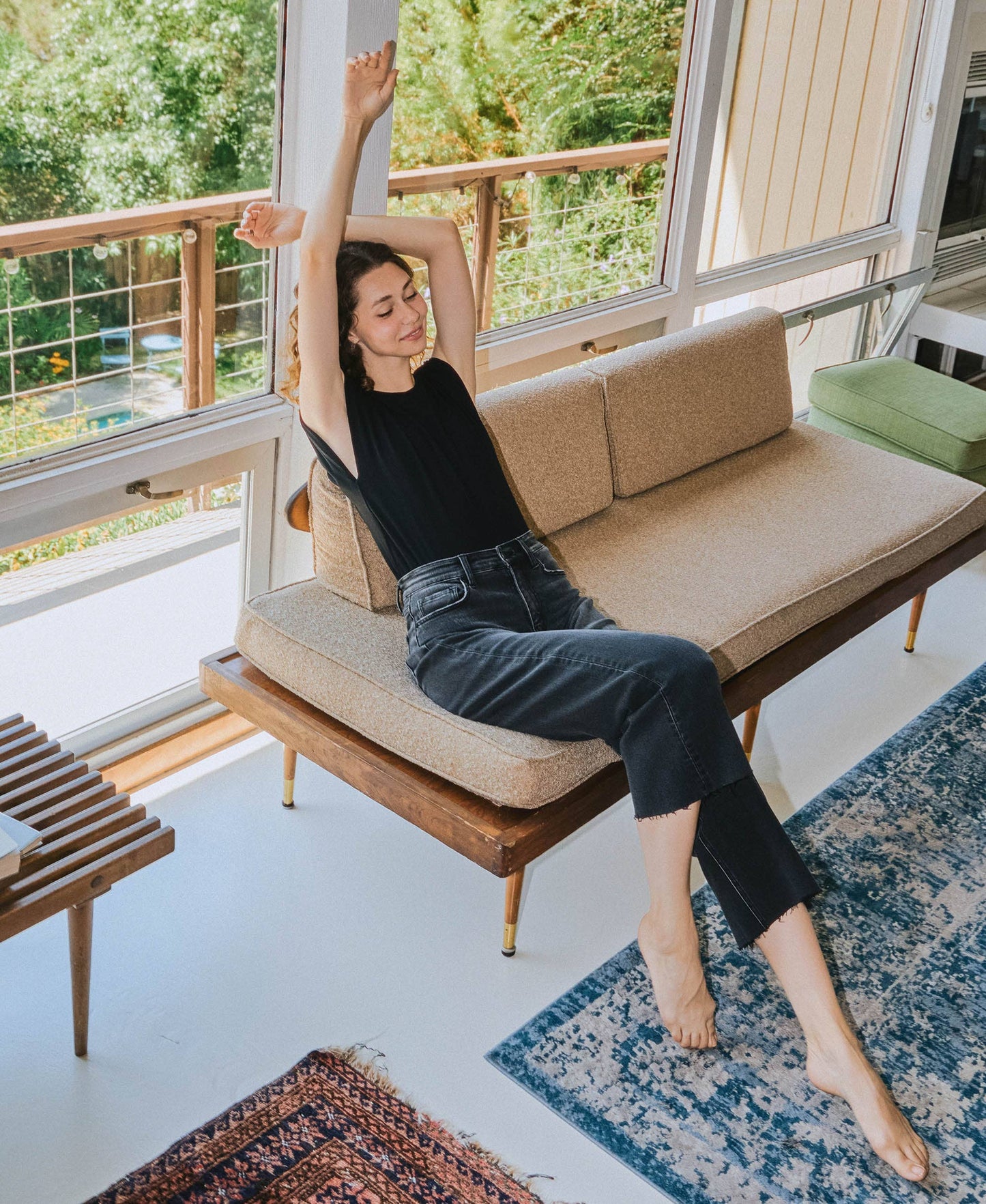 Woman stretching on a modern sofa in a bright living room with large windows.