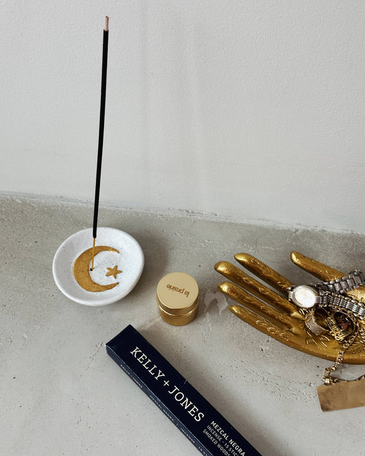Incense stick with a decorative dish on a concrete surface, next to a gold hand sculpture and a Kelly & Jones product.
