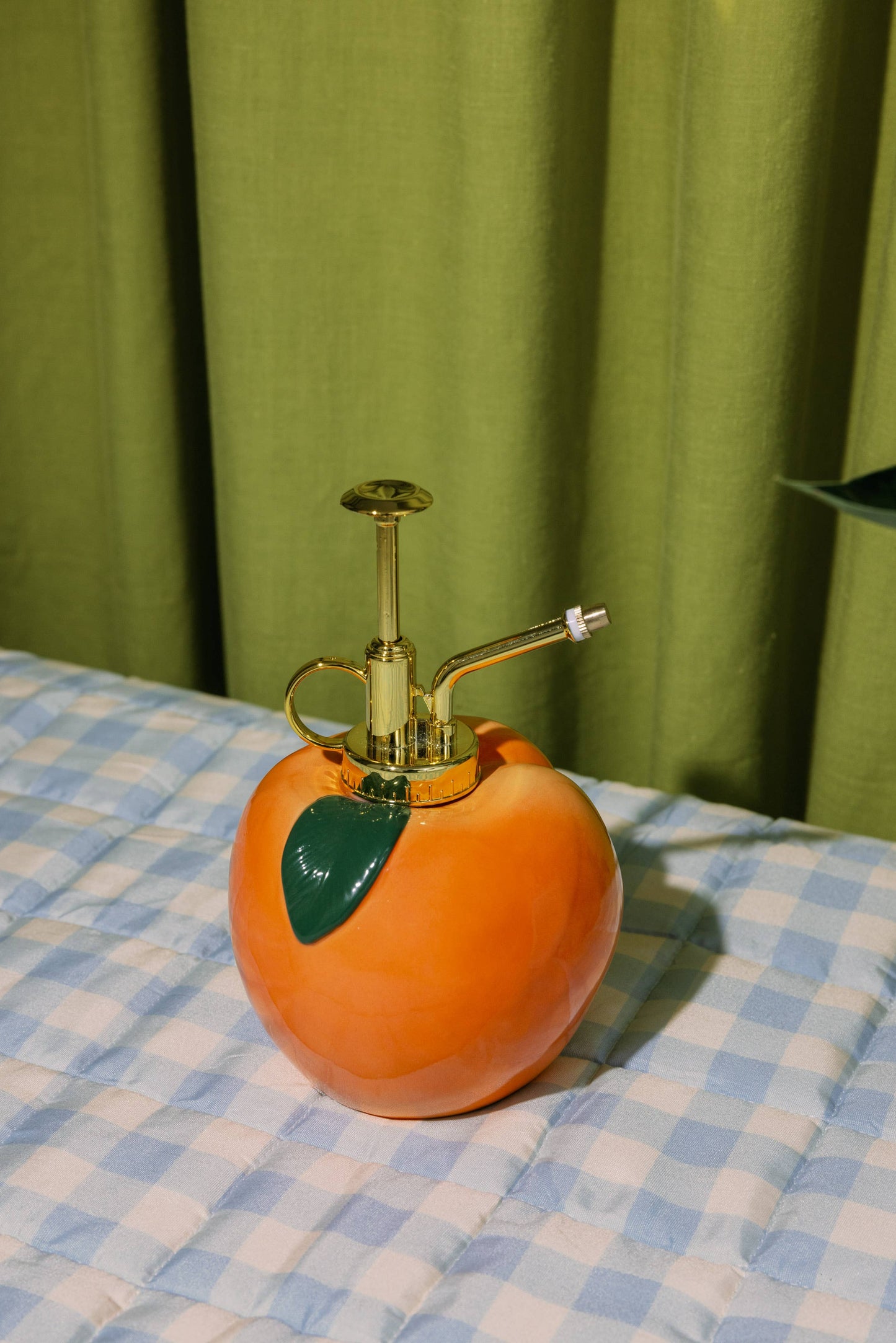 Peach-shaped spray bottle on a checkered tablecloth with a green curtain background