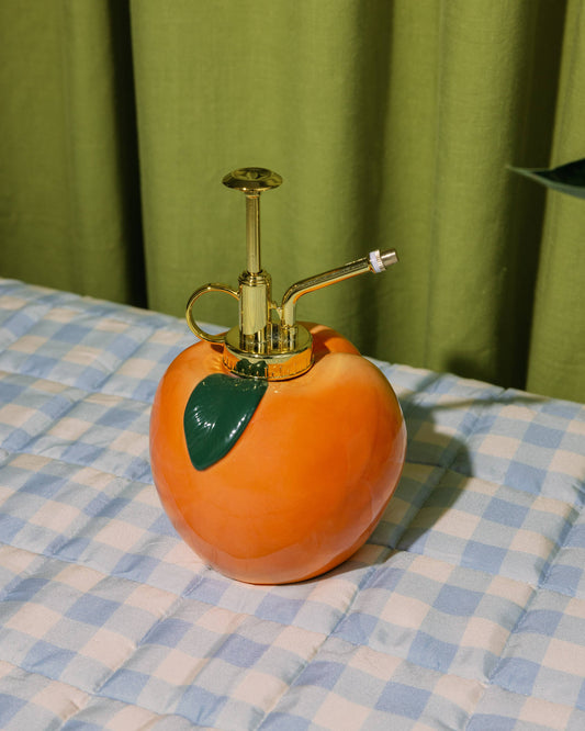 Peach-shaped spray bottle on a checkered tablecloth with a green curtain background