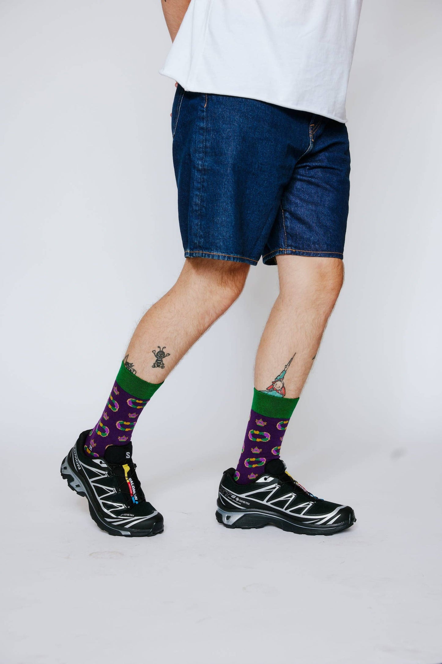 Person wearing blue denim shorts, colorful socks, and black sneakers on a white background