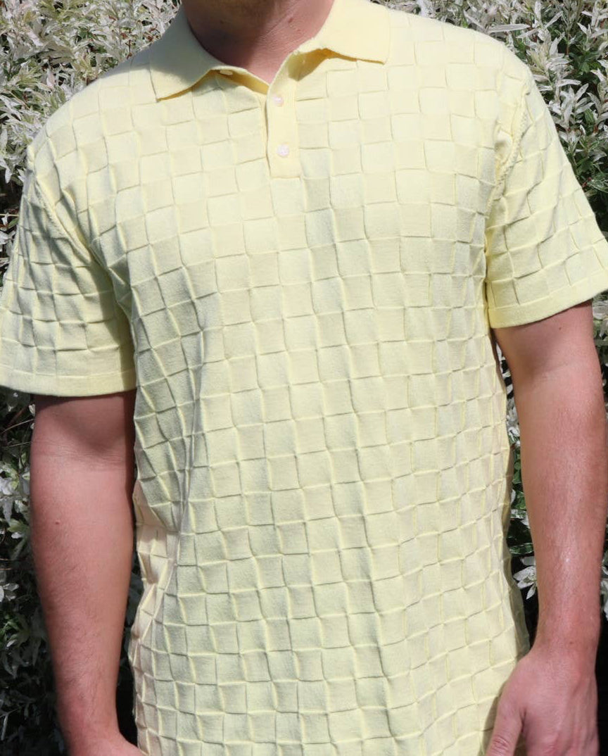 Person wearing a textured yellow shirt standing in front of a bush