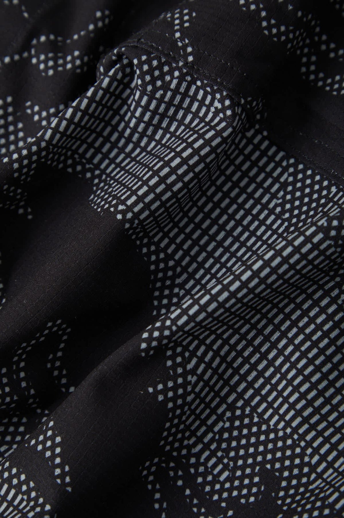 Close-up of a black fabric with a white geometric grid and dotted pattern, showing the material texture and folds.